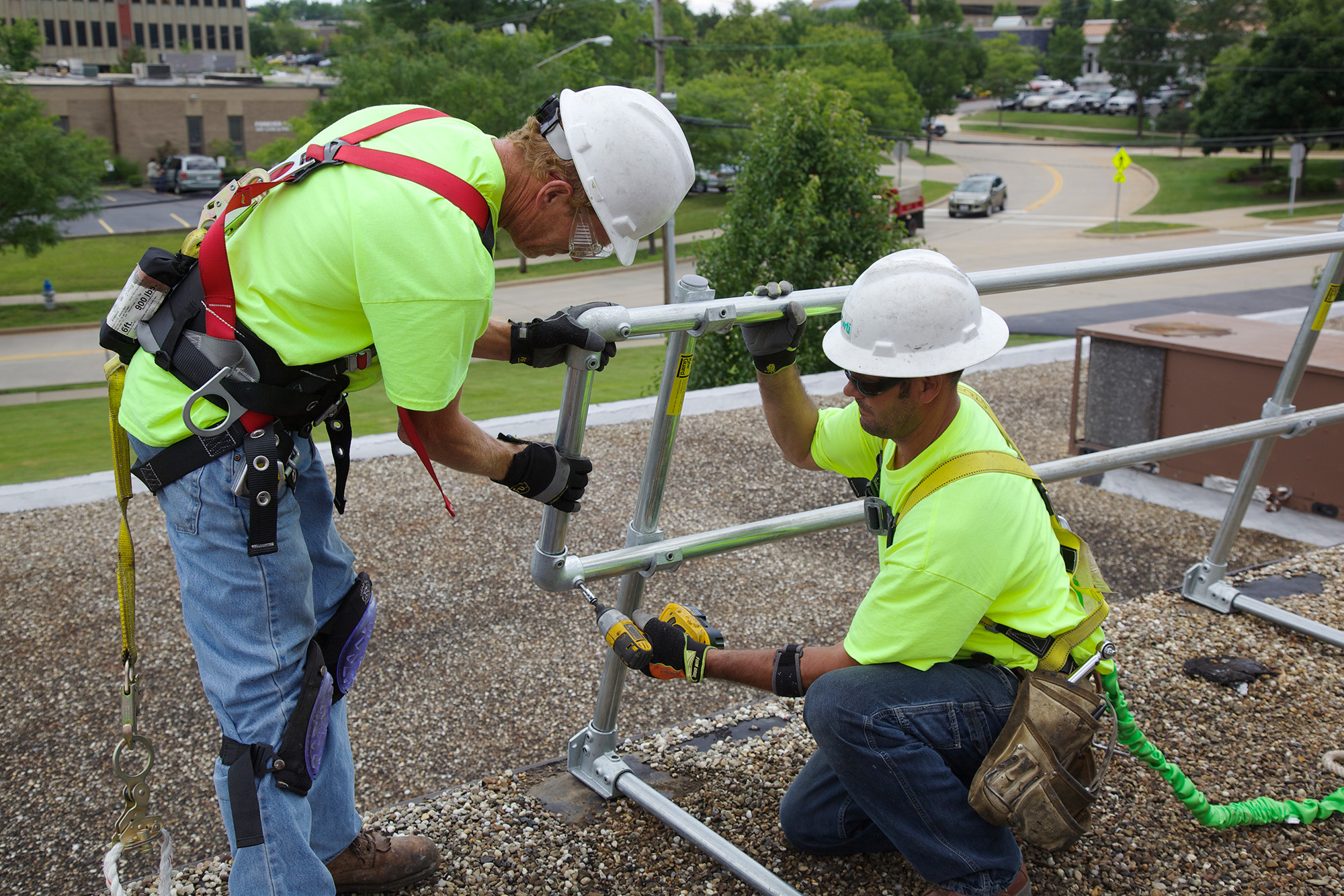 Two roofers installing a guard rail system on a roof.