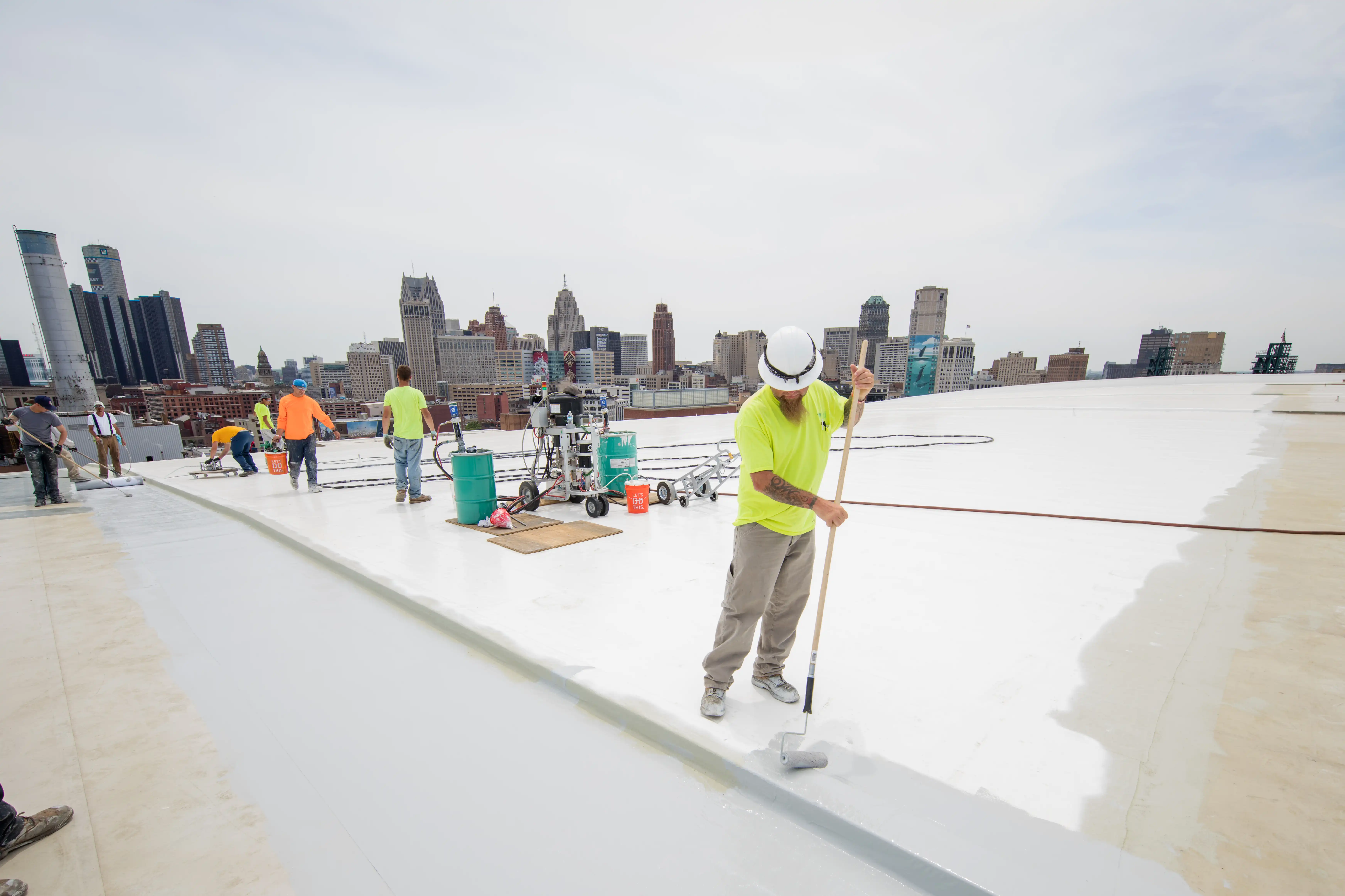 Installer rolls liquid membrane on a stadium rooftop with a city skyline in the background.